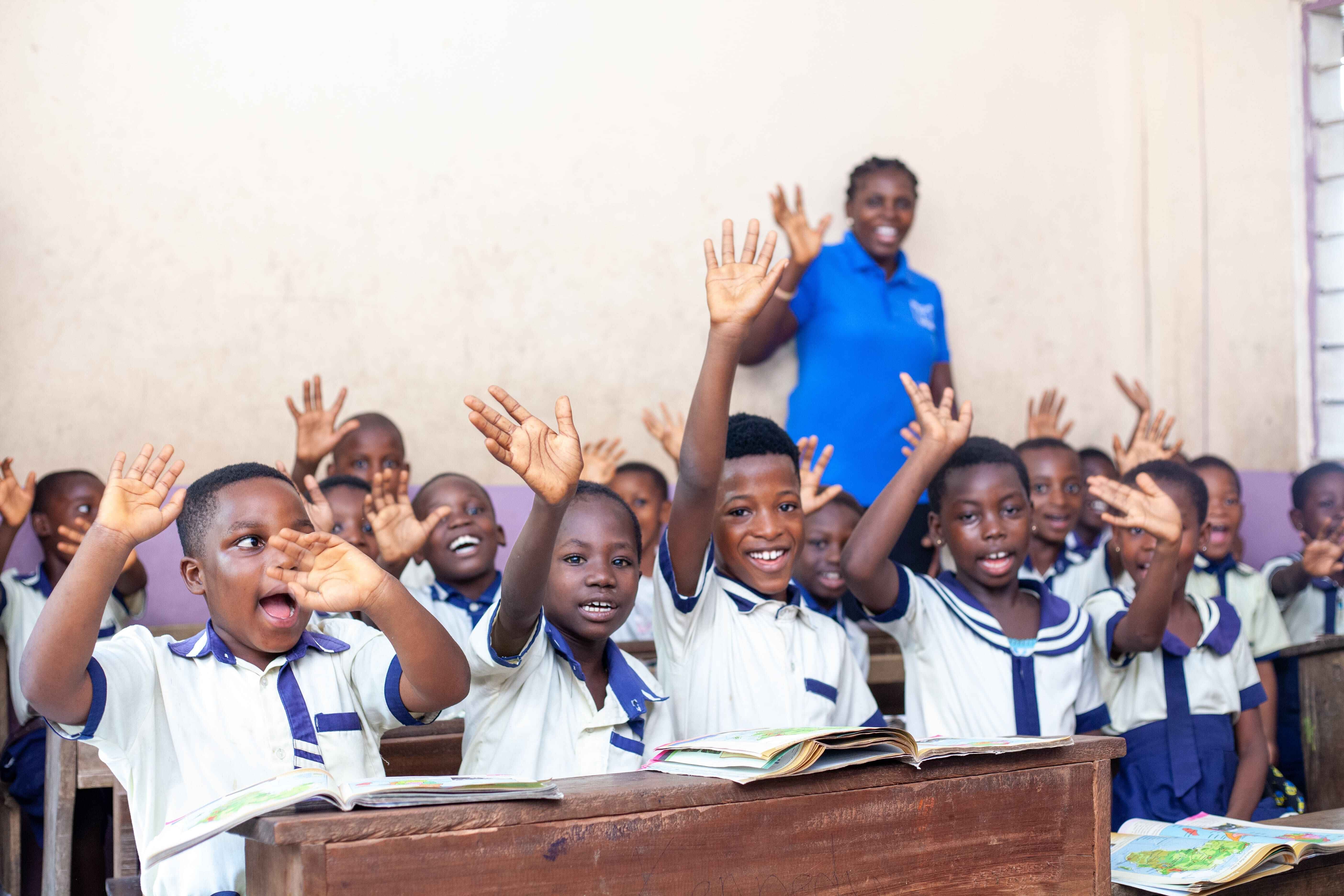 a group of children in a classroom with their hands up