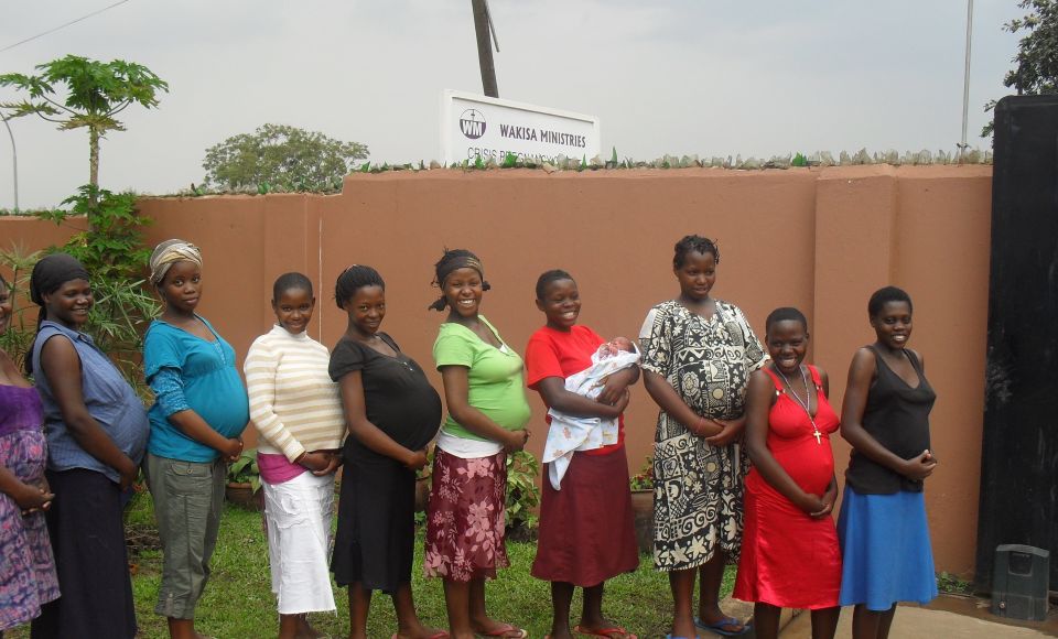 a group of nine pregnant ladies lined up in a line, smiling at the camera