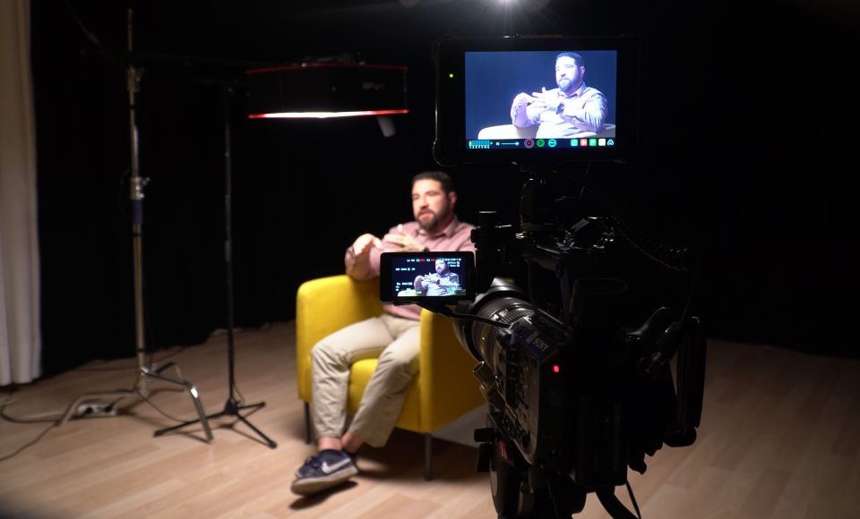 a young man sitting in a chair with a recording camera in front of him recording.