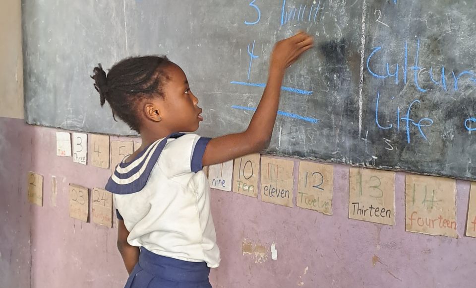 A young girl writing on a chalk board at school