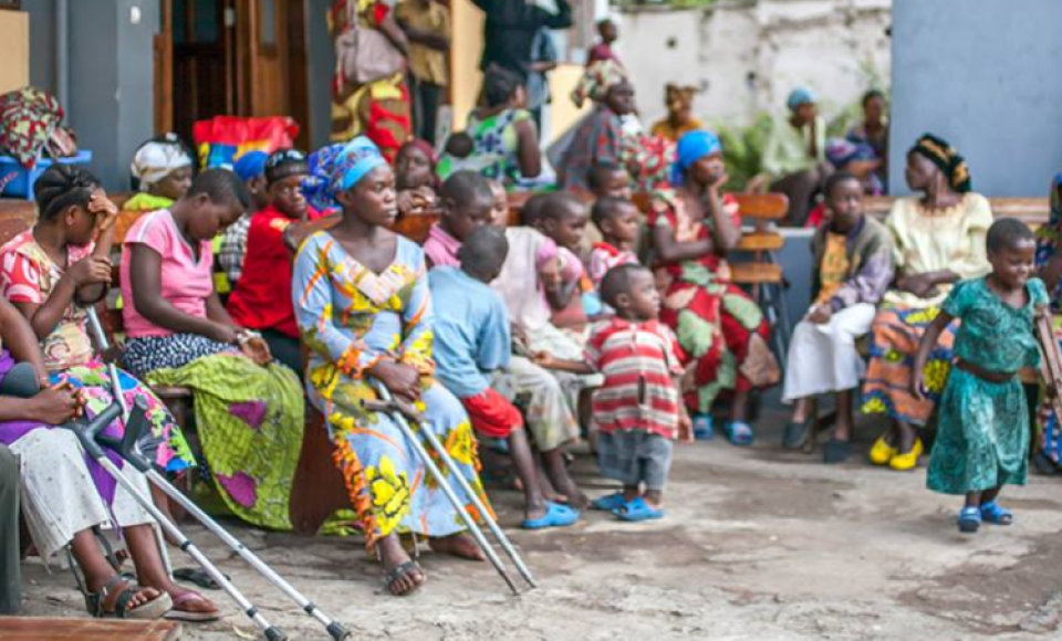 a large group of people sitting outside, a mixture of children and women.