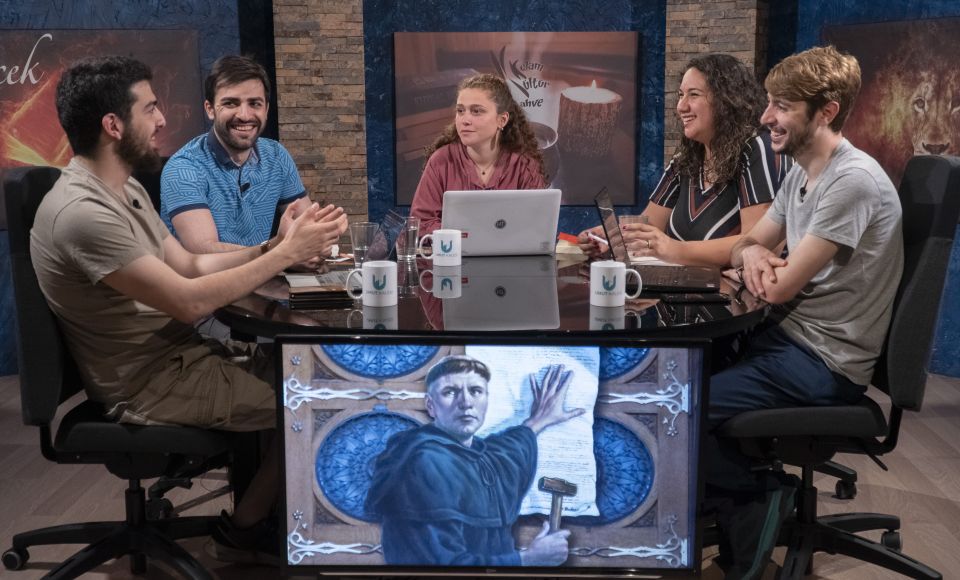 A group of five people sitting around a table, talking.