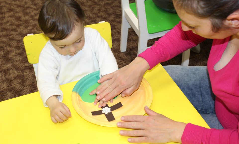 An infant child with an adult, practicing arts and crafts.
